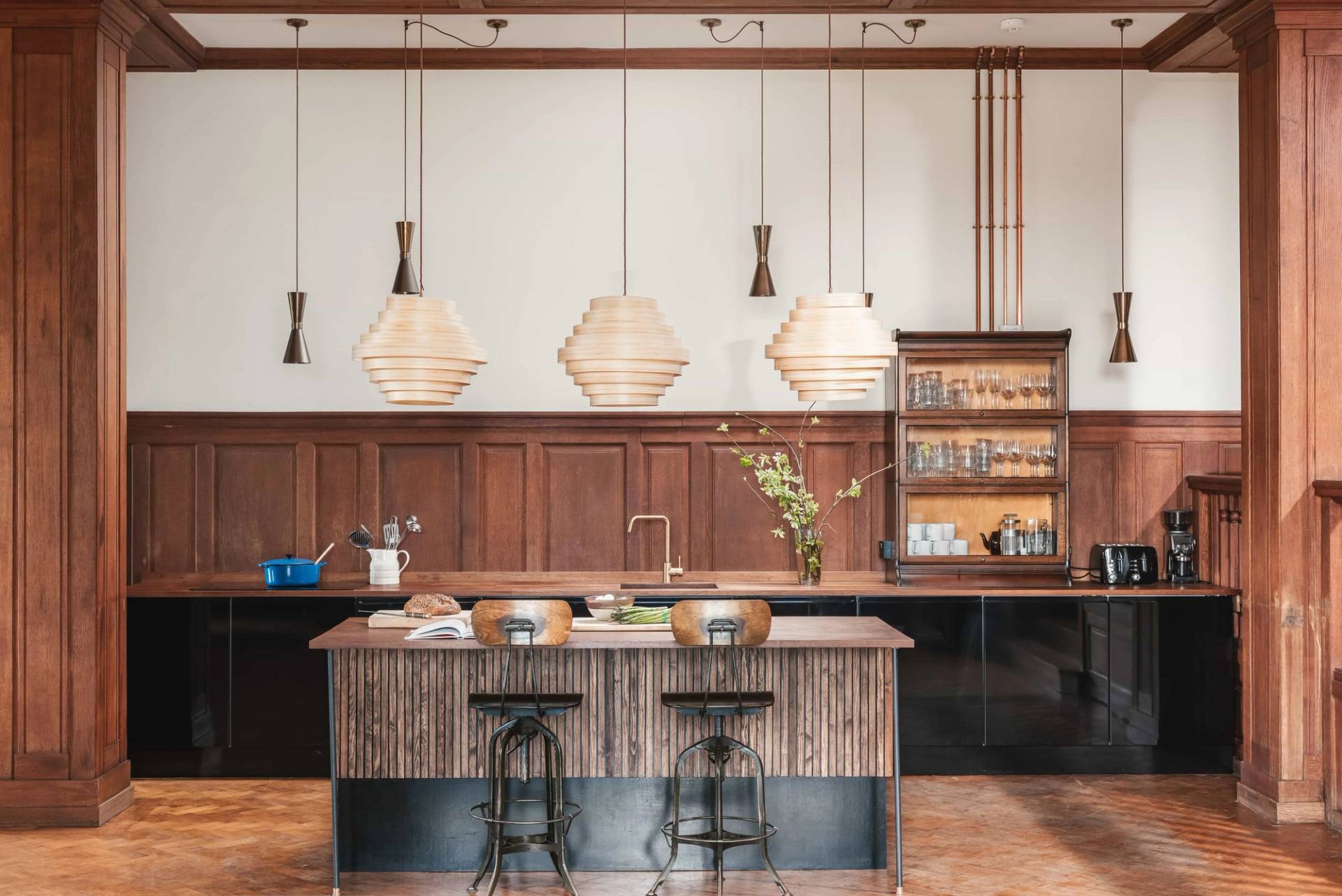 Luxury wood-panelled kitchen location in Ipplepen Totnes Devon TQ12 from Love Locations, featuring a rustic timber island counter, pendant lighting, and dark modern cabinets.