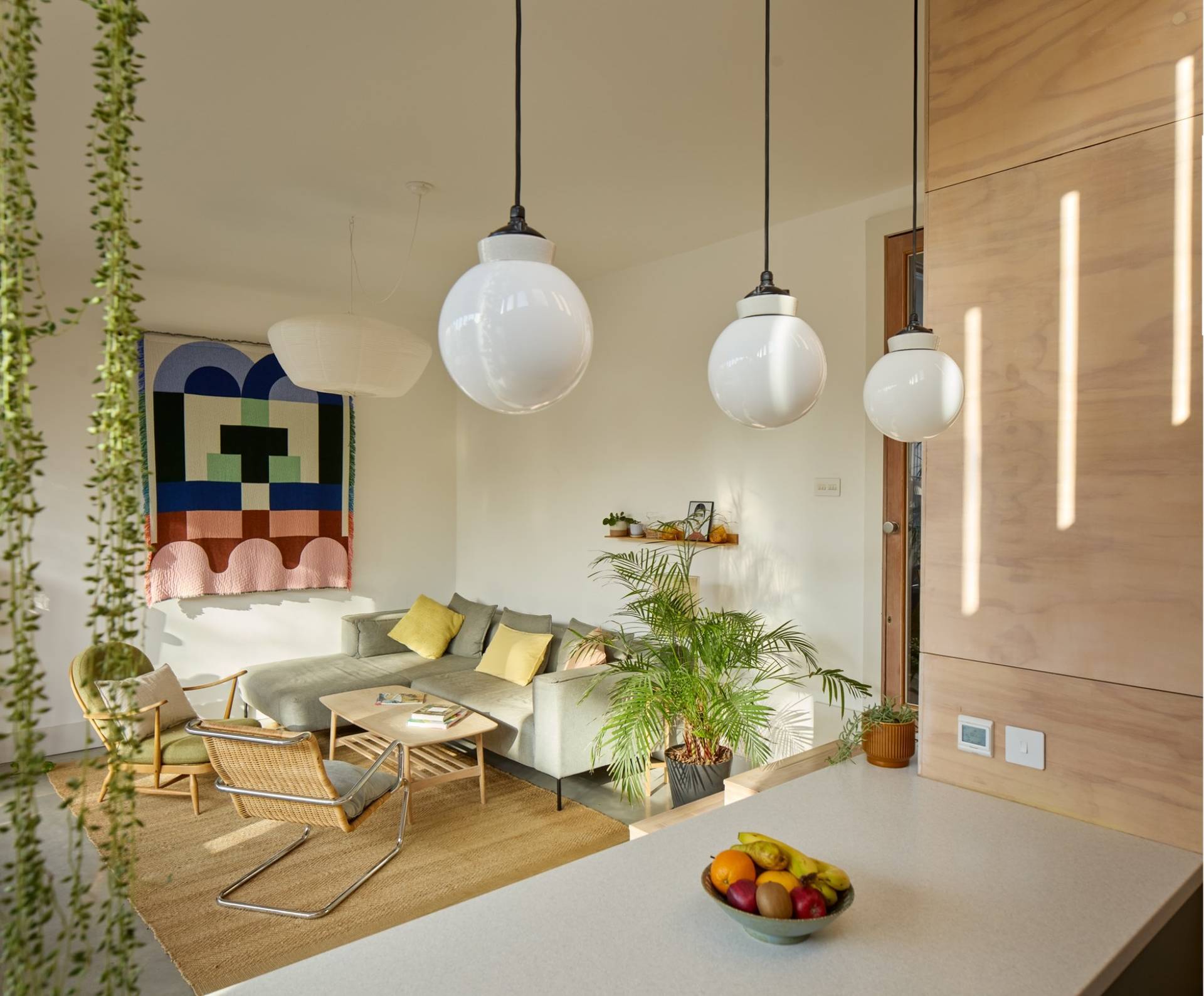 Plywood kitchen island detail with brass taps, pendant lighting, and modern living room furniture, Love Locations E17.