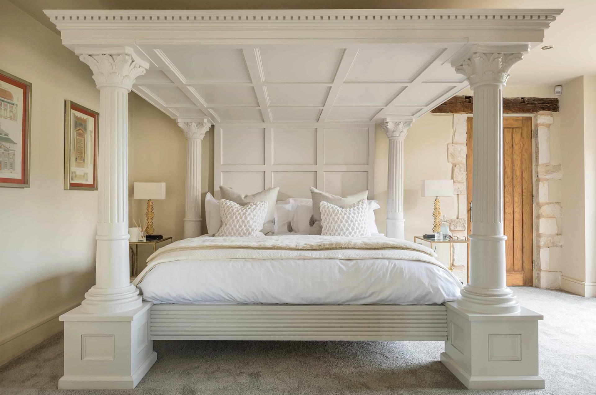 Romanesque-inspired master bedroom location house in Gloucestershire GL51 by Love Locations, featuring an ornate white four-poster bed, classical stone columns, and vaulted ceiling panelling.