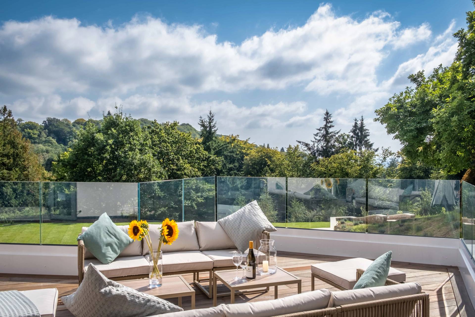 Elevated outdoor patio terrace with rattan lounge furniture, glass balustrade, and countryside forest views, perfect for summer campaigns, Love Locations GU27.
