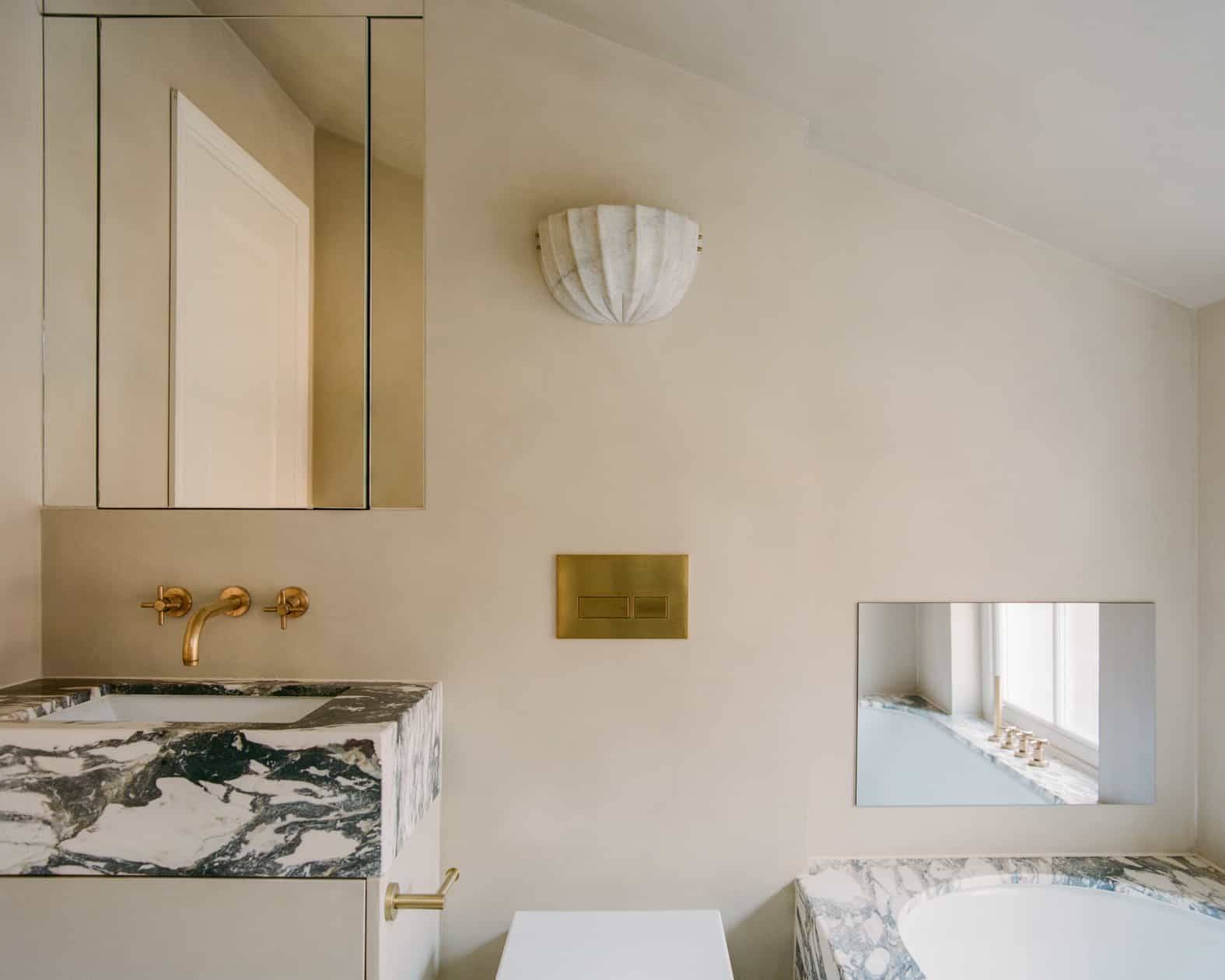 Luxury ensuite bathroom featuring green-veined marble vanity counter, brass taps, and micro-cement plaster walls, Love Locations SW4.