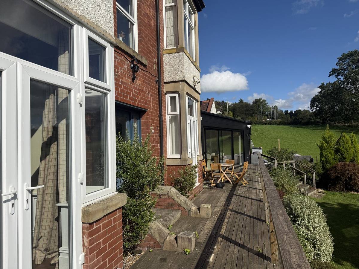 Exterior view of a red brick period house with an elevated timber balcony walkway in Stockport SK6 from Love Locations.