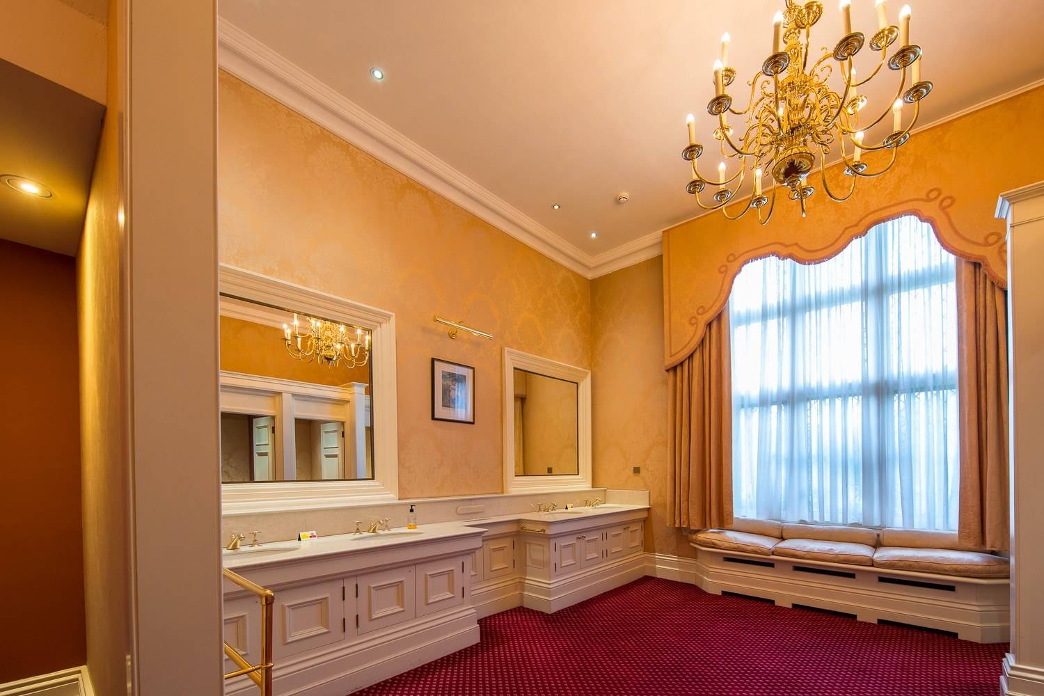 Luxury traditional bathroom shoot location featuring beige tiled walls, double vanity sink, and red carpet in Hertfordshire AL9 by Love Locations.