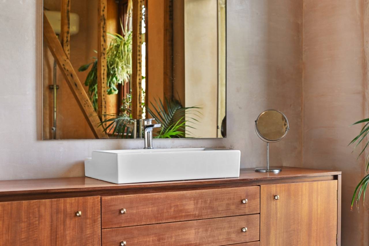 Close-up detail of a white vessel sink set on a mid-century wooden vanity cabinet, Love Locations E7.