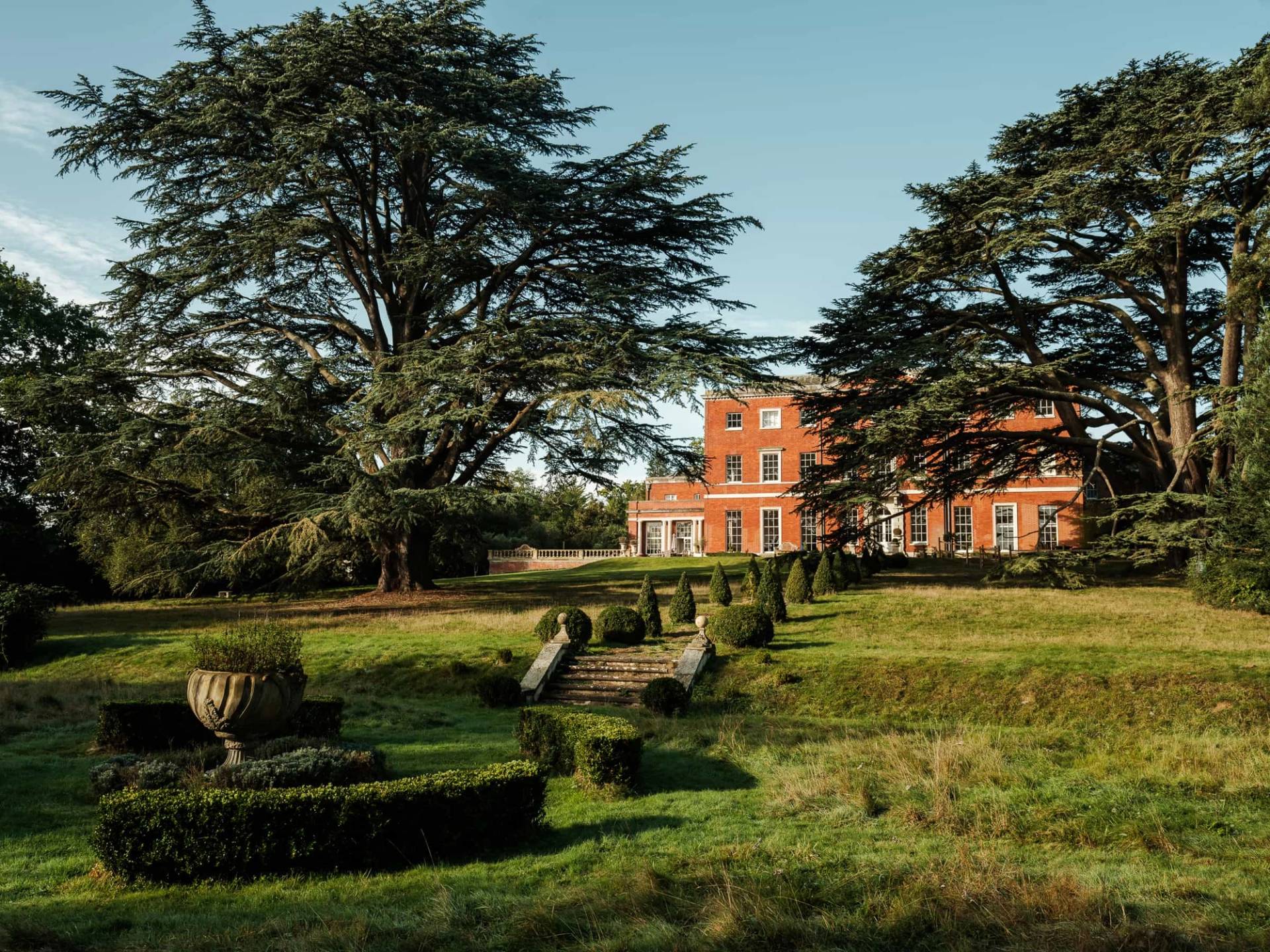 Elevated perspective of formal lawn gardens, terraced steps, and a red brick Georgian mansion facade, Love Locations RG42.