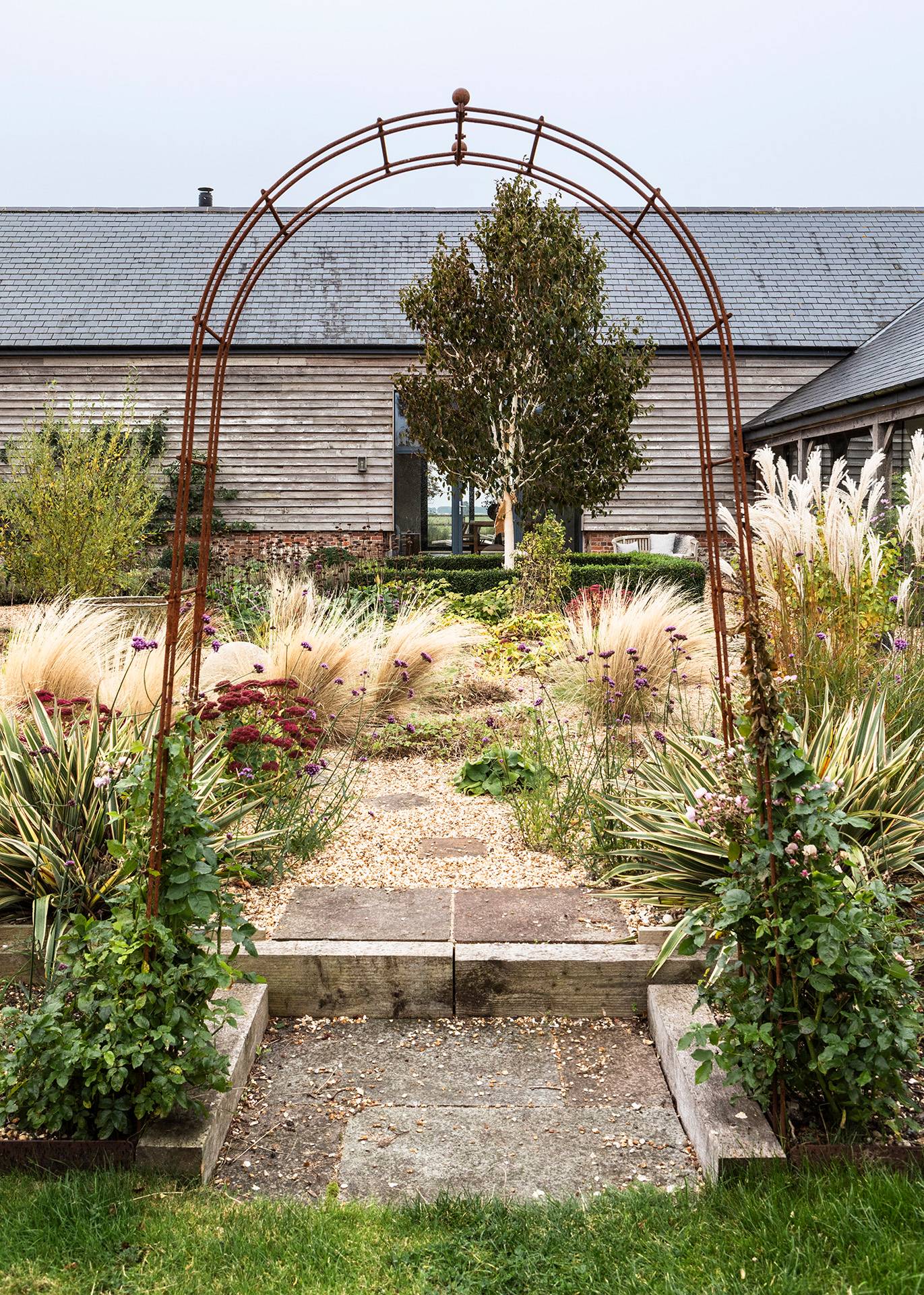Gravel garden walkway framed by decorative metal archways and tall ornamental grasses in Wiltshire, Love Locations SN8.