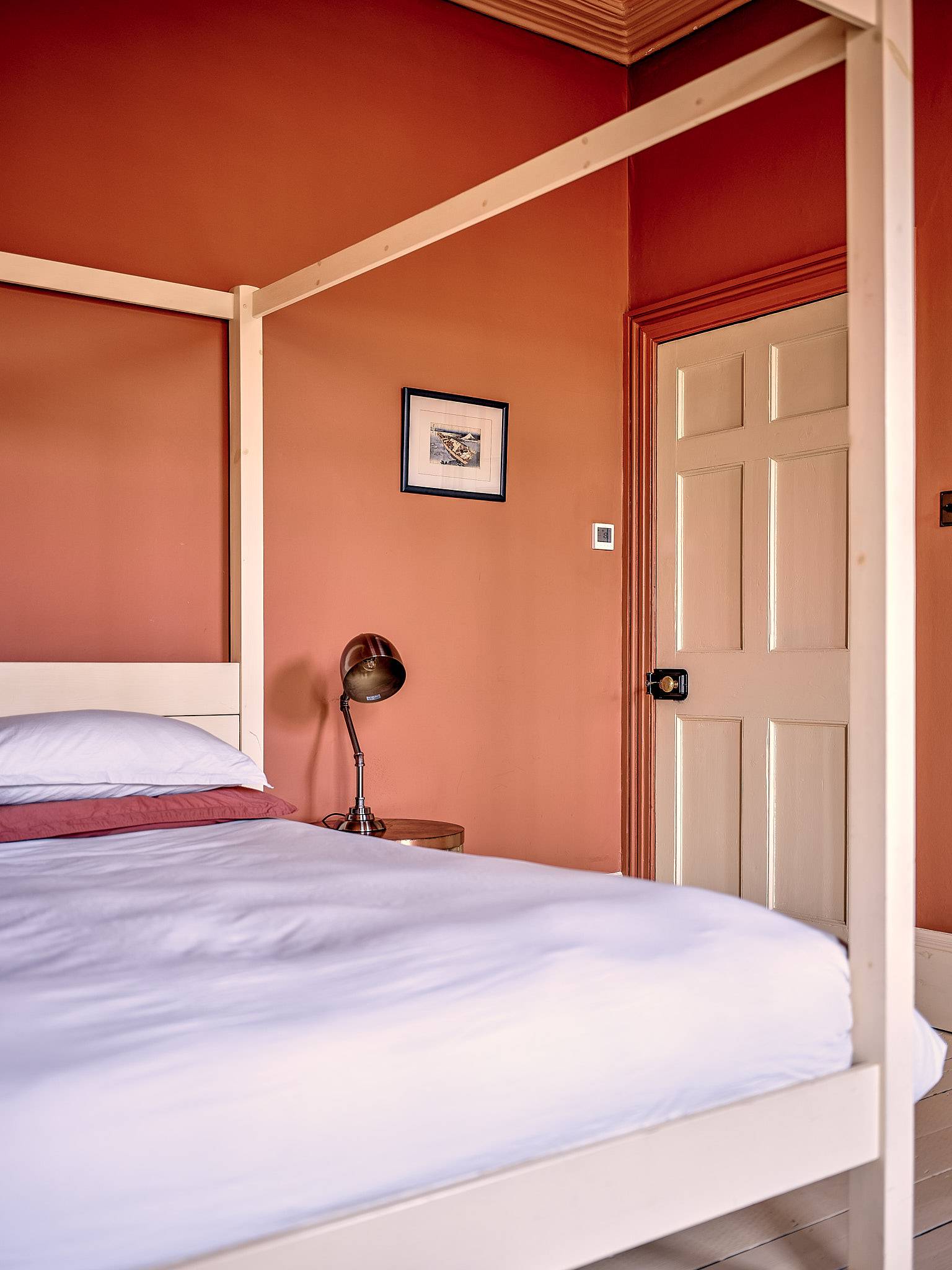 Minimalist timber four-poster bed set against terracotta orange walls in a Faversham location house, Love Locations ME13.