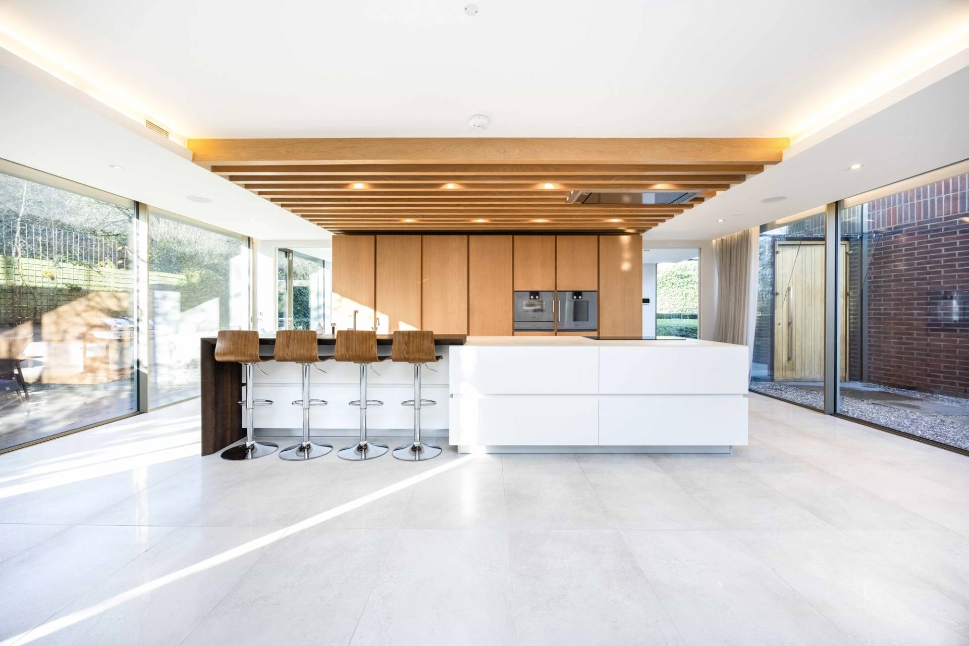 Modern kitchen bar with white waterfall counter, chrome bar stools, and wood panelled cabinetry in Radlett, Love Locations WD7.