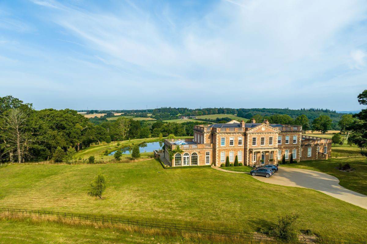 Elevated panoramic view of the Greentrees manor house sitting proudly within its 170-acre Sussex valley landscape, Love Locations.