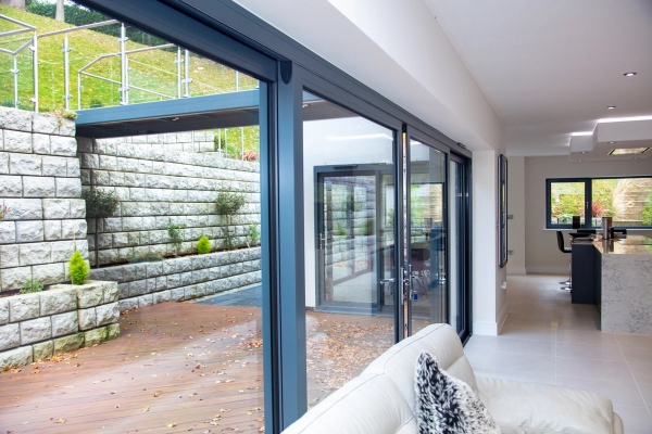Close-up view of premium sliding glass patio doors framing a manicured hillside stone garden wall backdrop, Love Locations Surrey.