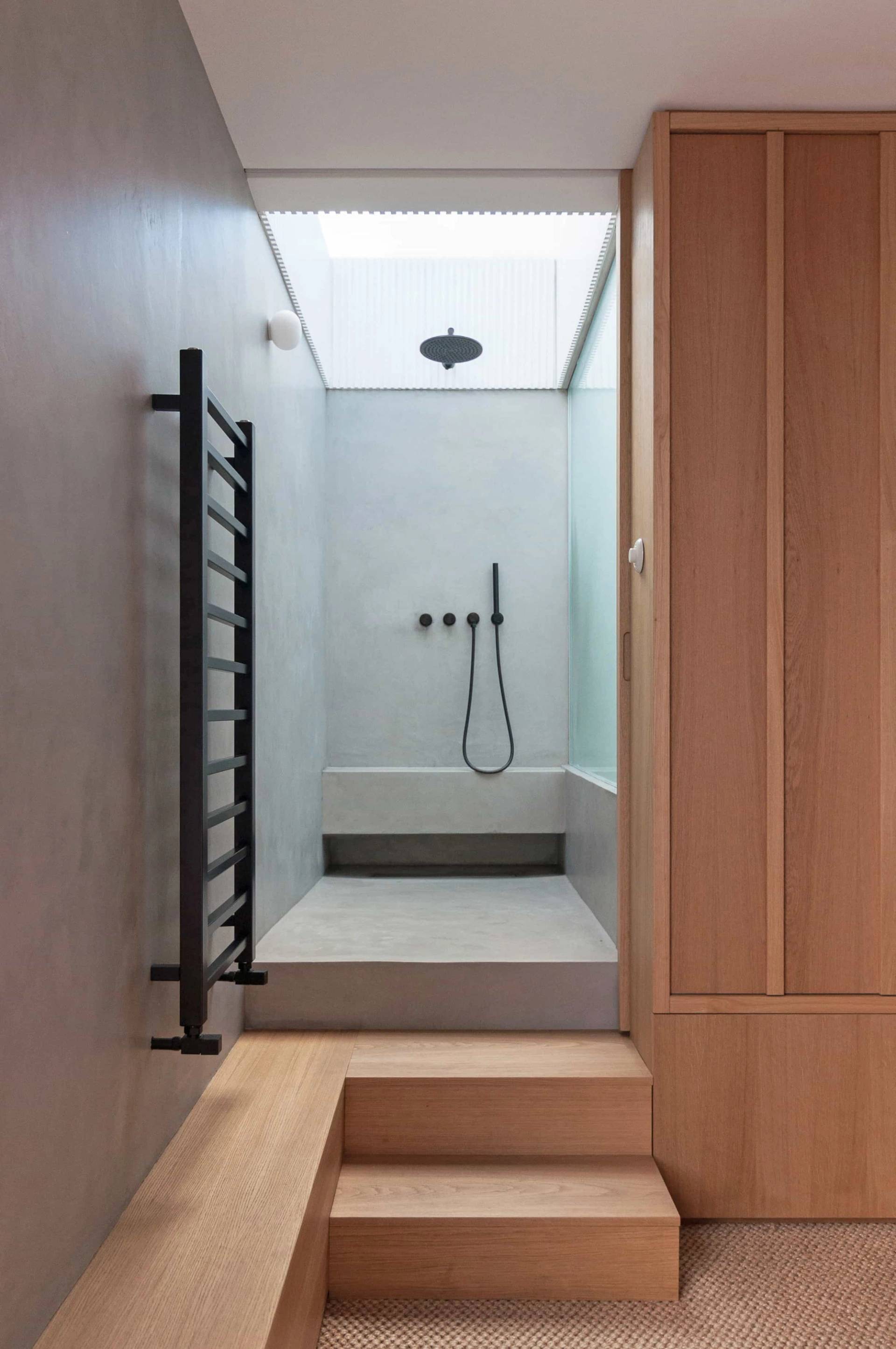 Minimalist wet room shower location house in Hackney N16 by Love Locations, displaying a sunken shower tray, skylight, and black heated towel rail.