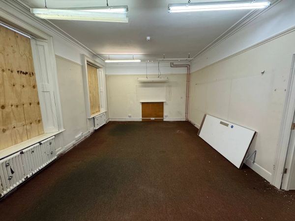 Large empty room inside an abandoned mansion filming location featuring boarded windows and stained carpets in Beeston, Nottingham, NG9 via Love Locations.