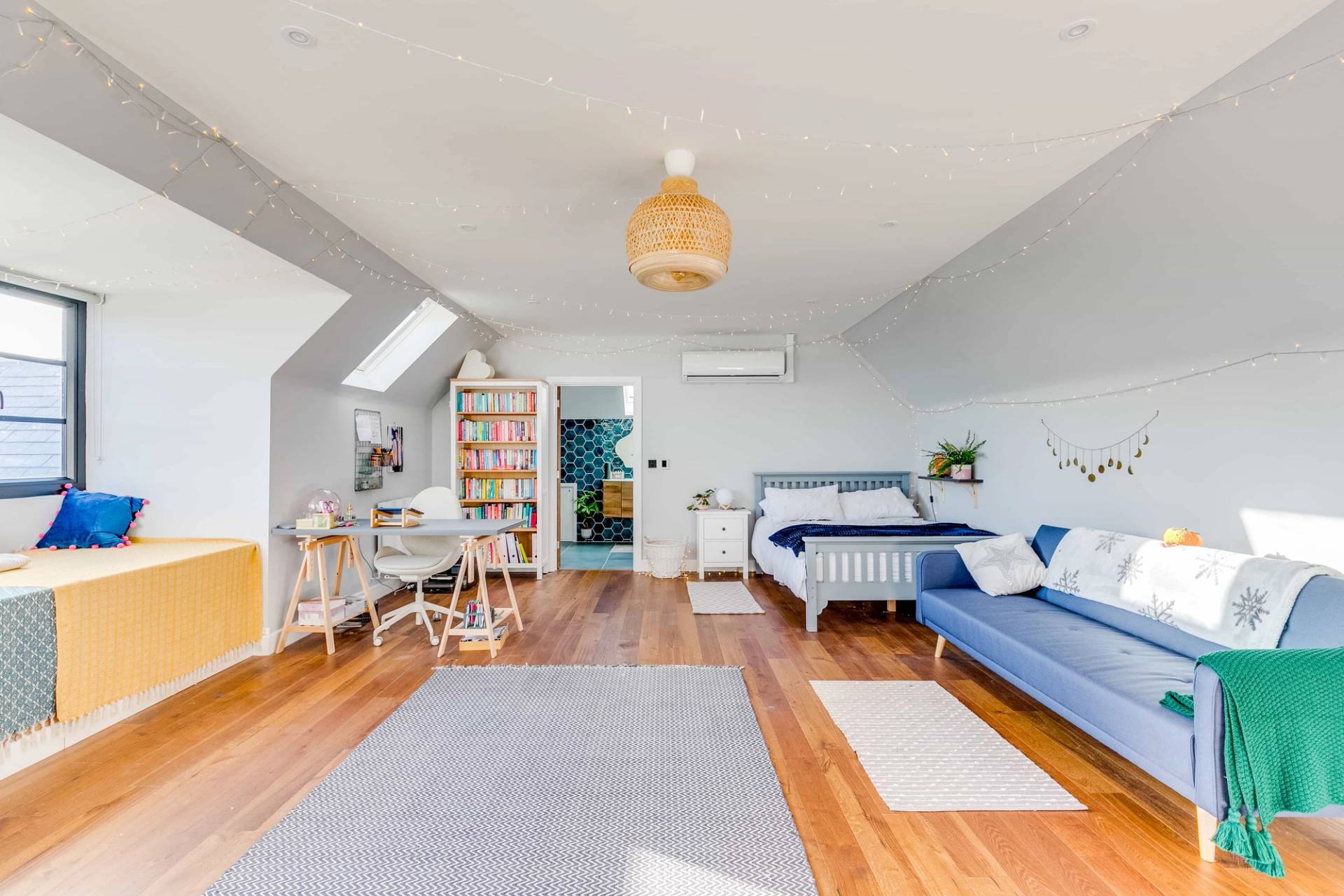 Spacious attic loft bedroom suite featuring wooden flooring, sloped ceiling, blue sofa, and desk area, Love Locations CB2.