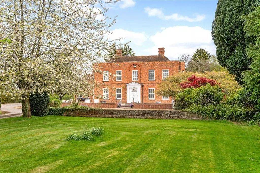 Stately red-brick Georgian manor house exterior facade viewed across manicured green lawns via Love Locations.