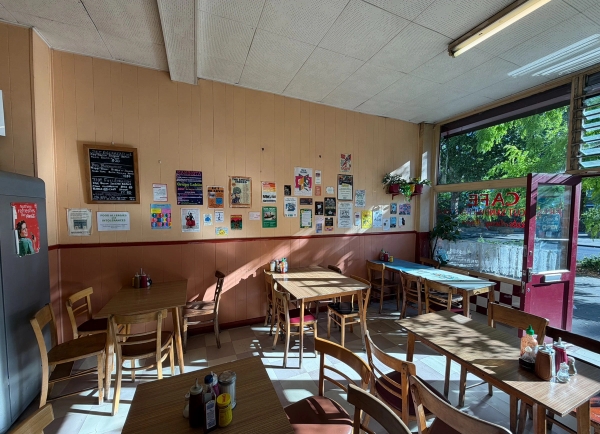 Classic cafe dining room interior with wooden tables, chairs, wall notices, and warm sunlight streaming through glass shopfront windows, Love Locations SE27.