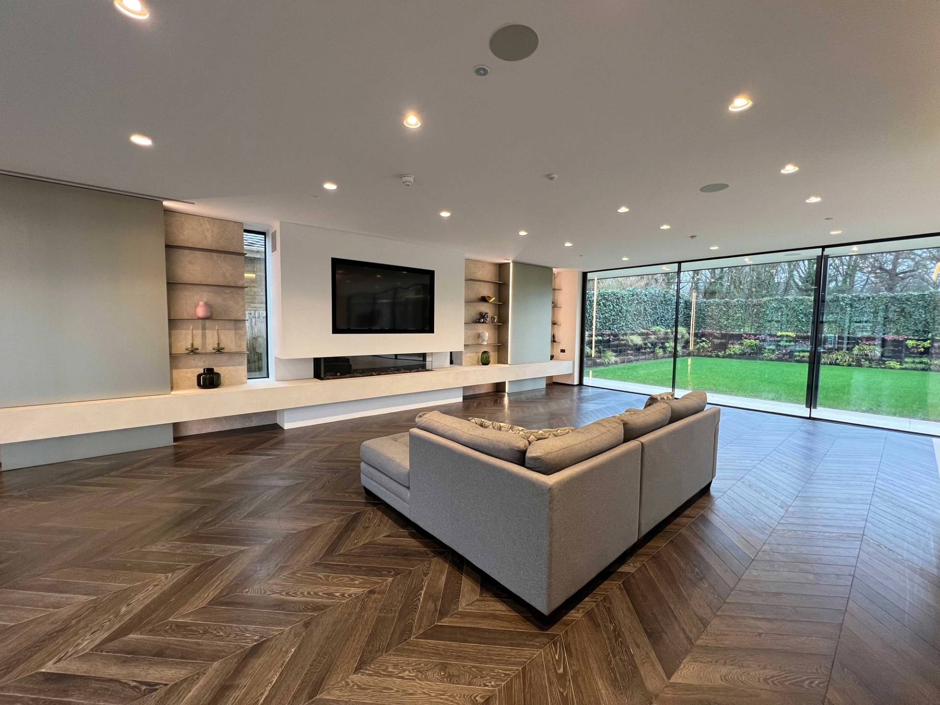 Spacious open-plan reception room with dark herringbone parquet floors, neutral L-shaped sofa, and recessed ceiling lighting, ideal for family lifestyle campaigns, Love Locations.