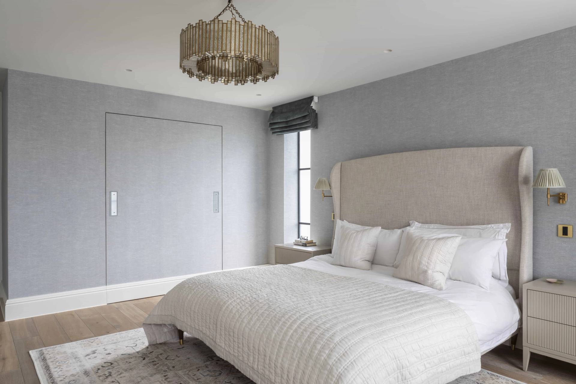 Neutral master bedroom featuring a grey upholstered bed, round chandelier, and sash window light, Love Locations HP18.