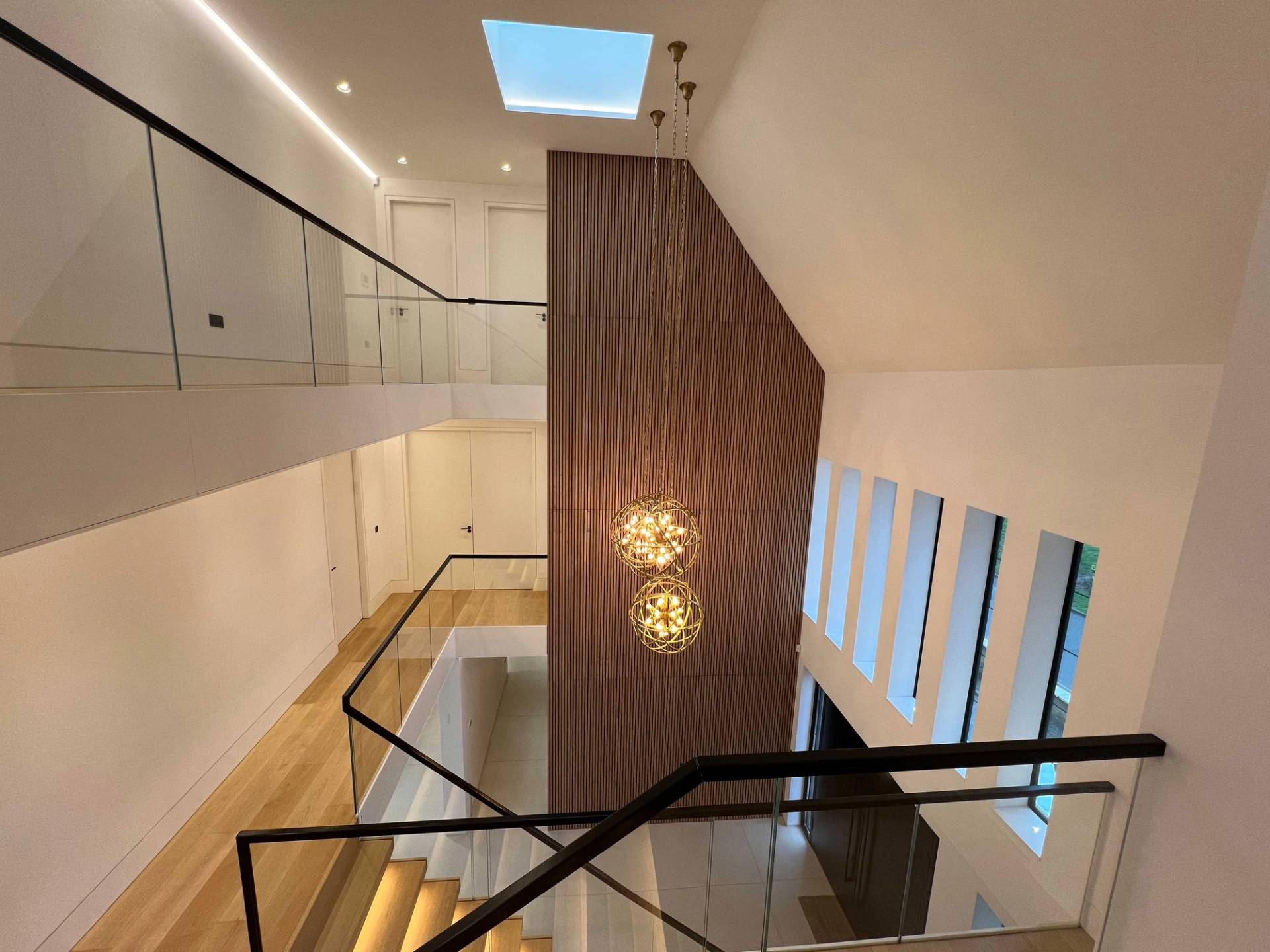 High-angle perspective from an upper glass balcony looking down into a double-height entrance hall with globe chandeliers, Love Locations.