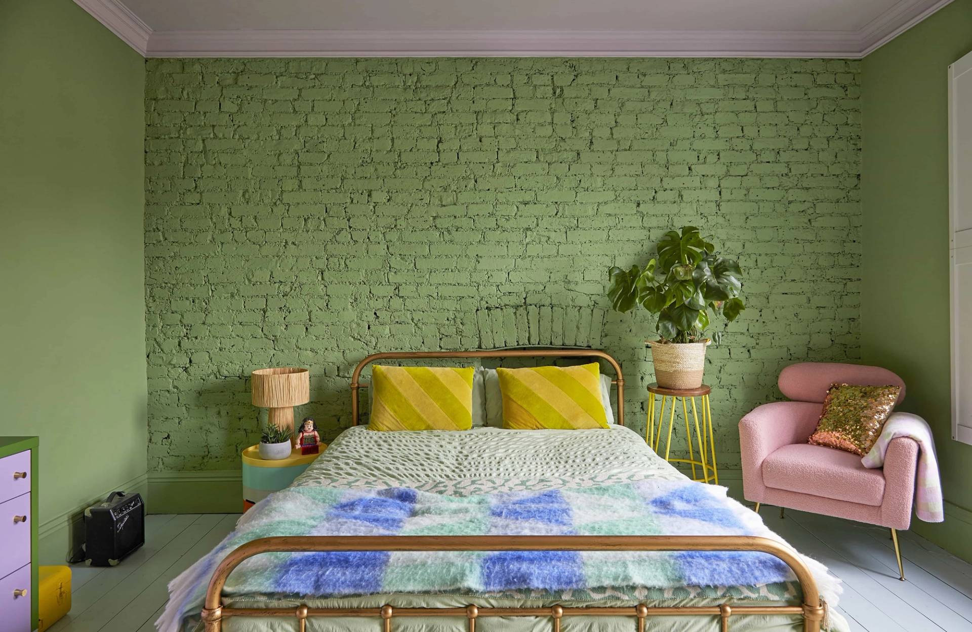 Pistachio green bedroom setup featuring an iron bed frame, green brick feature wall, and yellow bedside lamps, Love Locations SE6.