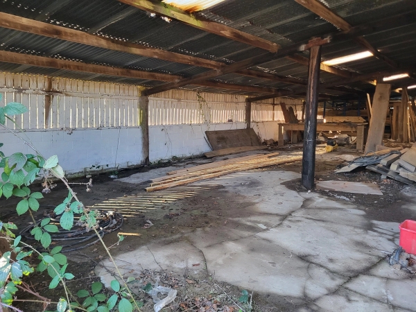 Rustic open-plan barn shelter with dirt flooring and corrugated metal roof panels, Love Locations BN8.