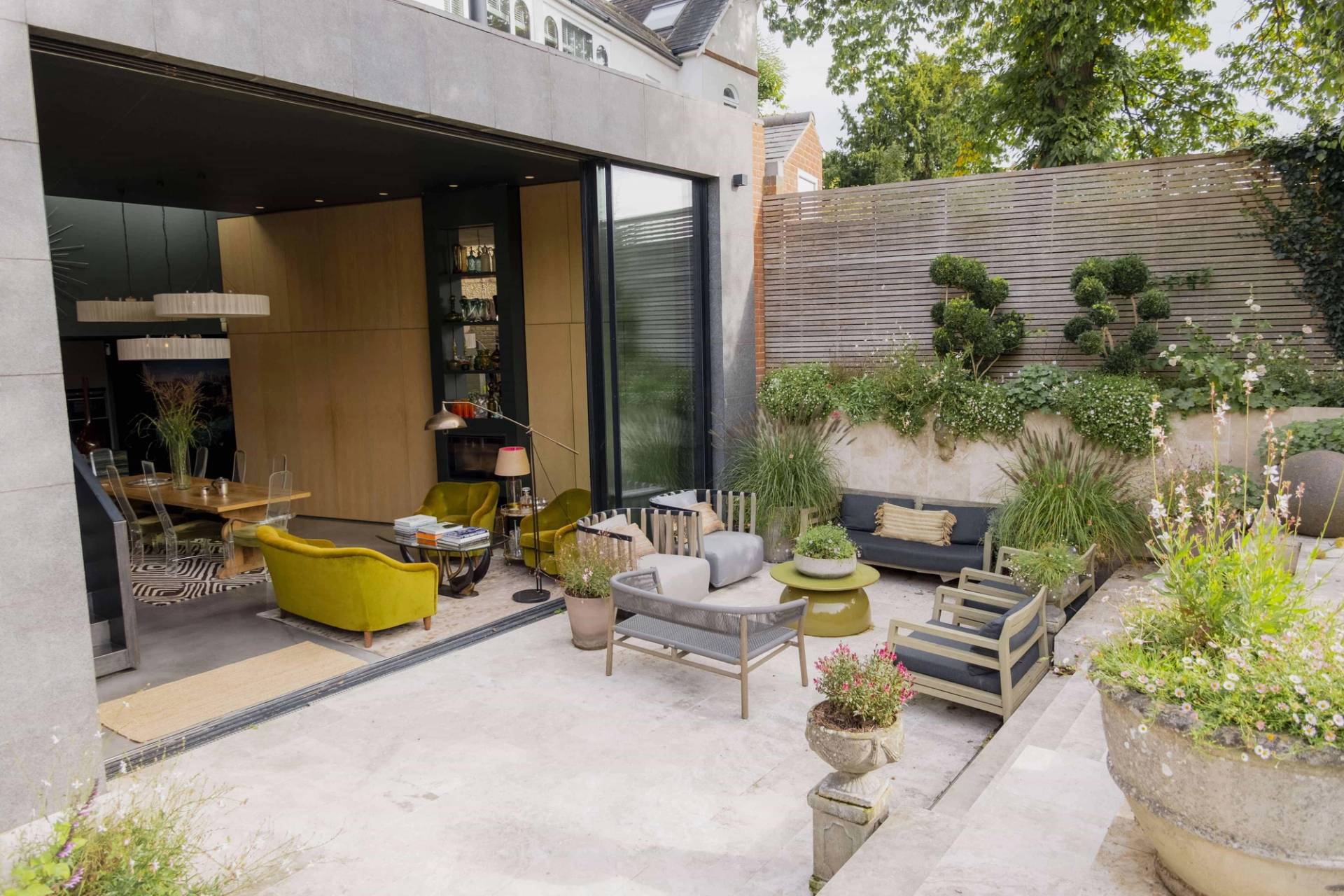 Paved outdoor courtyard patio featuring casual lounge seating and stone retaining walls set against a modern glass extension in Wimbledon, SW20, Love Locations.