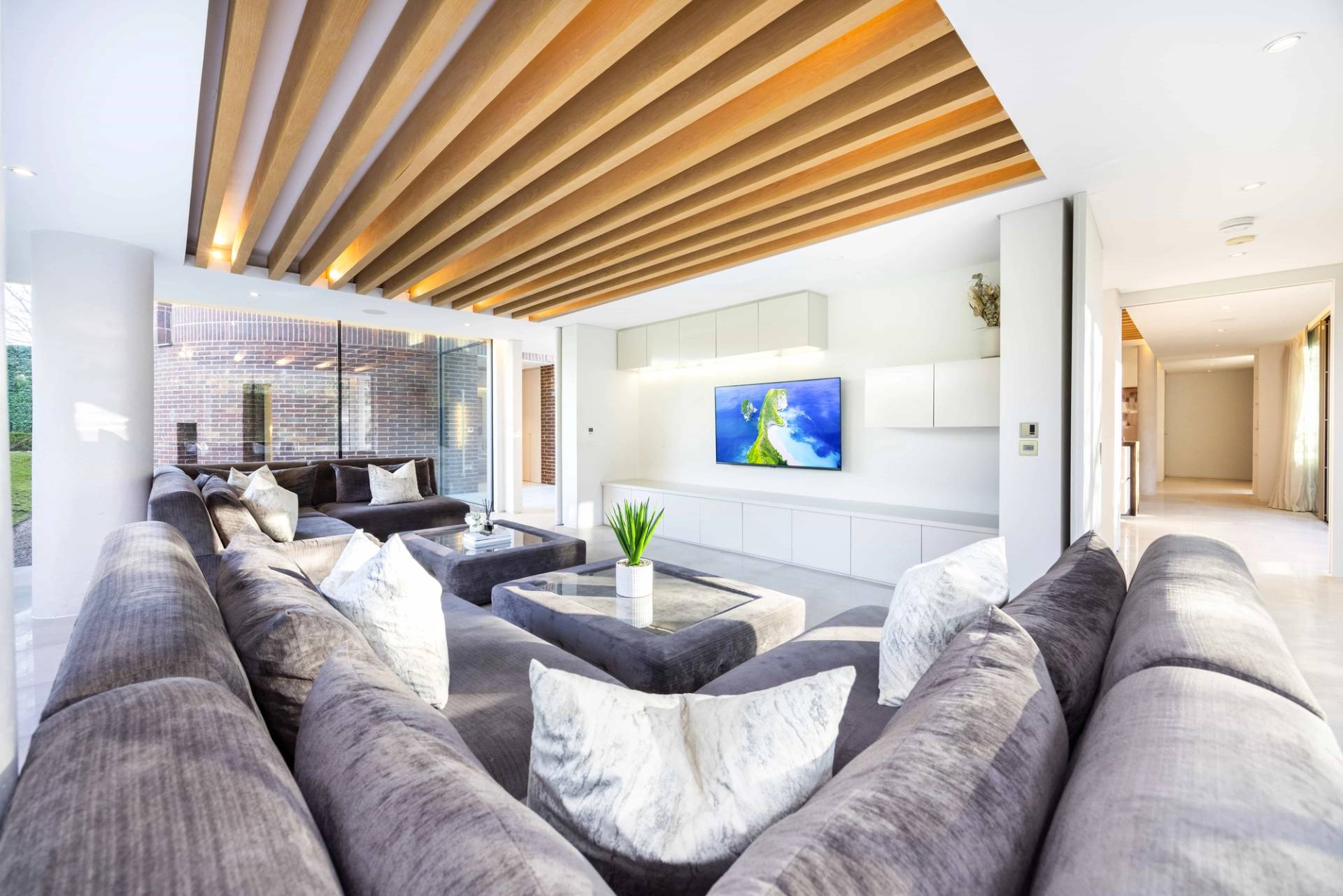 Modern lounge area with slatted timber ceiling, plush sectional sofa, and recessed wall television, Love Locations WD7.