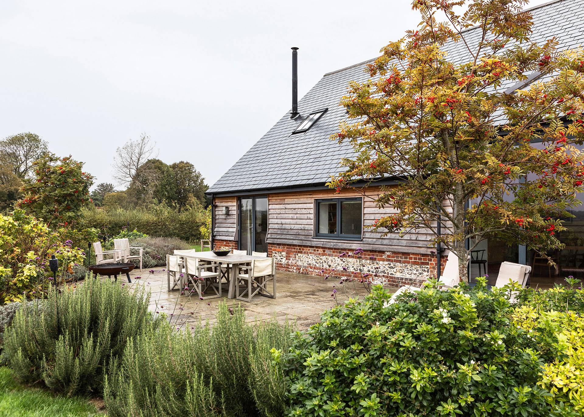 Paved outdoor dining patio set outside a modern weatherboard barn conversion with stone tables, Love Locations SN8.