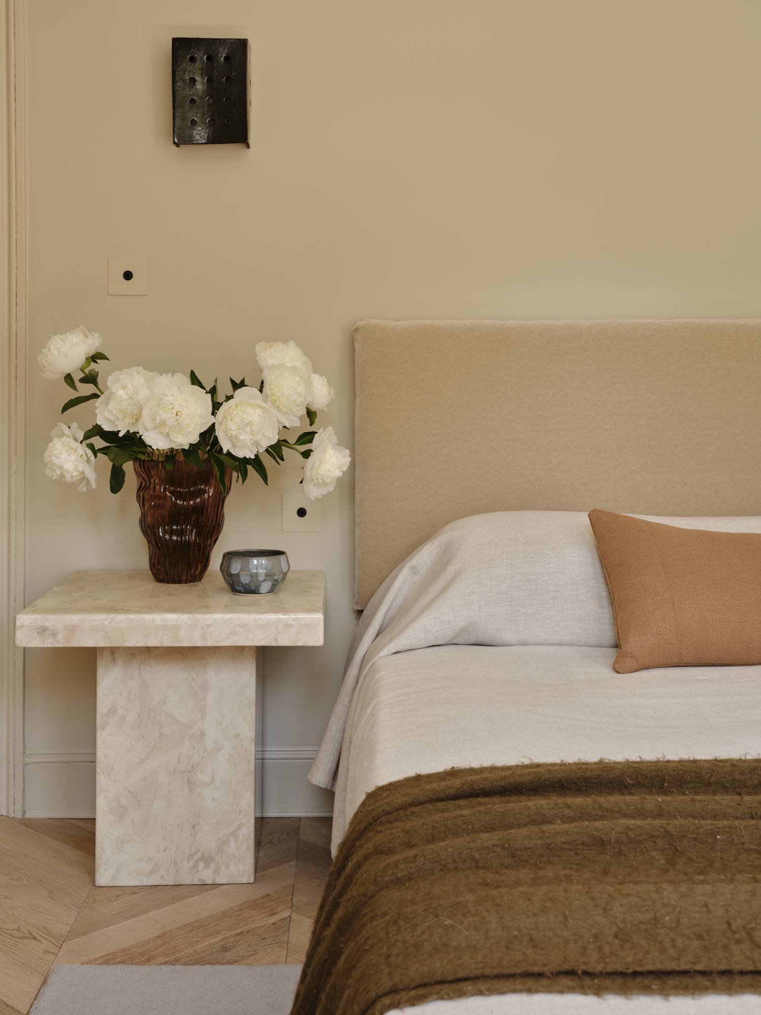 Love Locations calm aesthetic bedroom Lewisham: Serene double bedroom layout showcasing a plush beige headboard and a monolithic travertine stone bedside cube, perfect for bedding shoots.