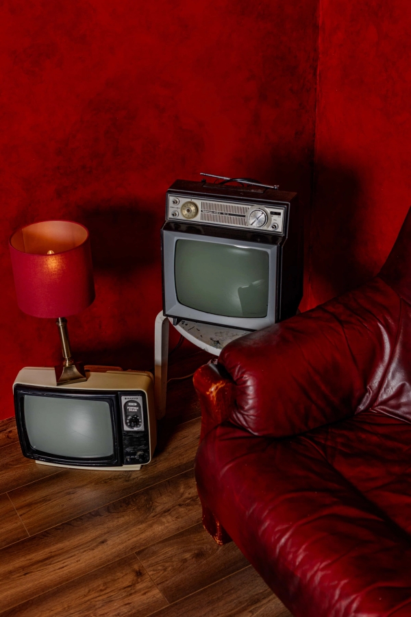 Close-up detail of retro stackable CRT television monitors beside a red leather sofa on a red studio set, Love Locations N15.