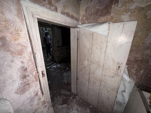 Distressed doorway looking into a dark, empty room with crumbling brickwork and decaying plaster, listed on Love Locations.