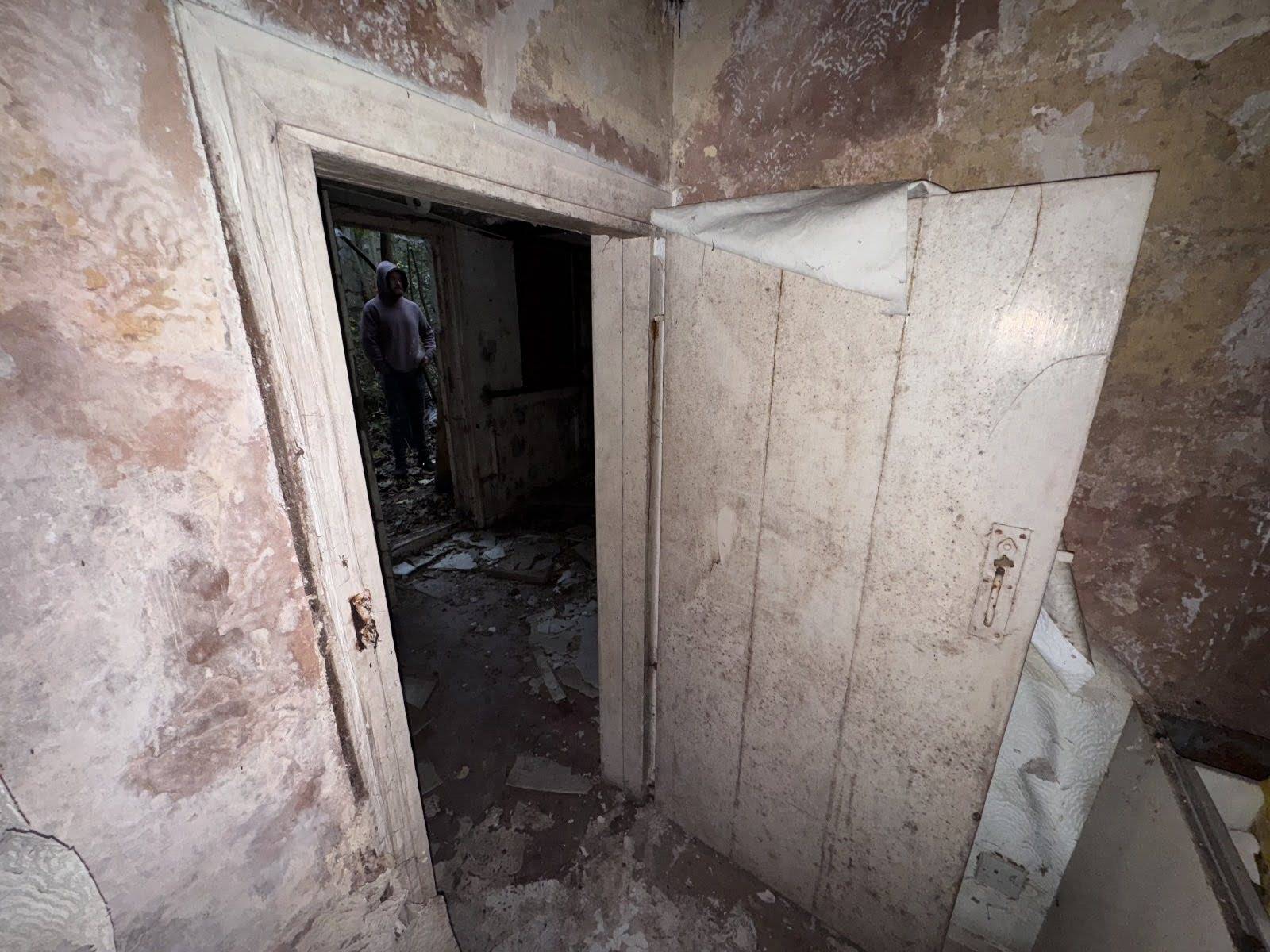 Distressed doorway looking into a dark, empty room with crumbling brickwork and decaying plaster, listed on Love Locations.