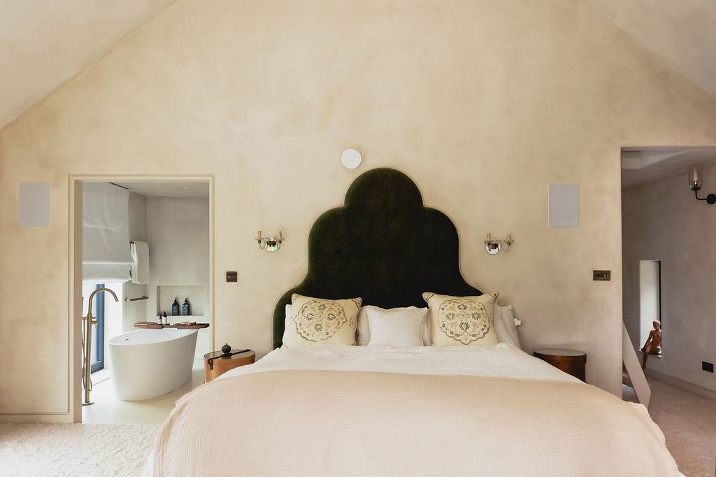 Master bedroom suite with a black upholstered scalloped headboard, neutral bedding, and microcement walls, Love Locations GU32.