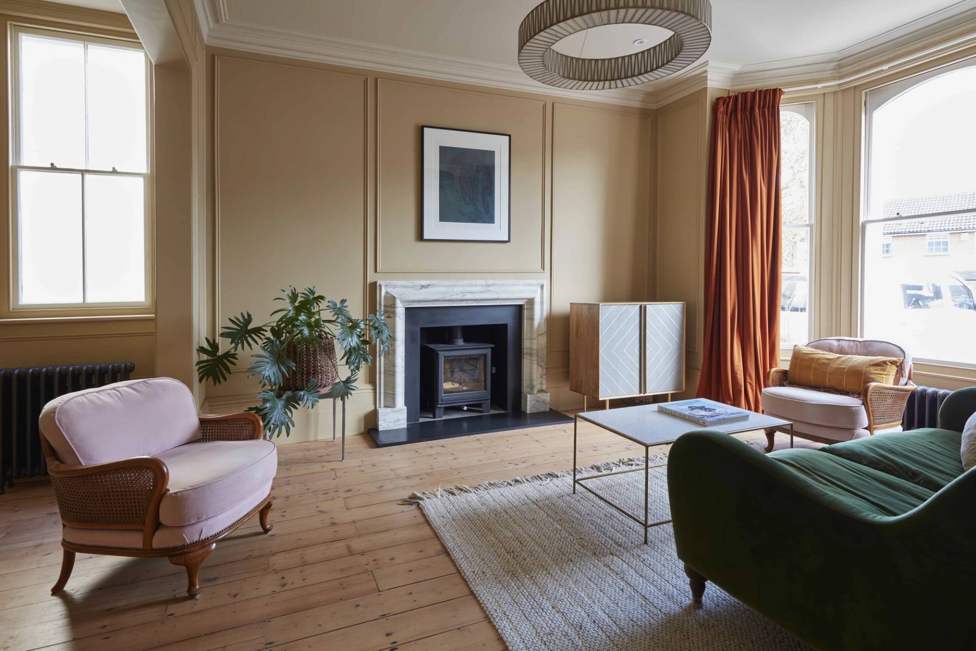Spacious lounge room with ochre wall panelling, dark floorboards, and a marble fireplace hearth, Love Locations.