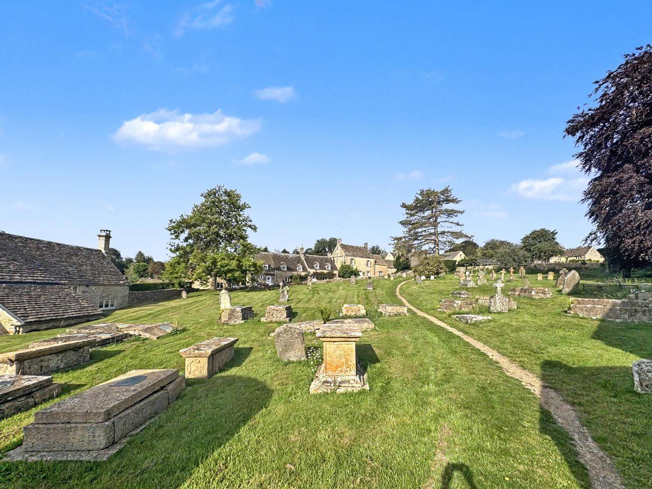 Historic churchyard pathways and gravestones filming location in Gloucestershire GL7 via Love Locations, surrounded by open skies and village views.