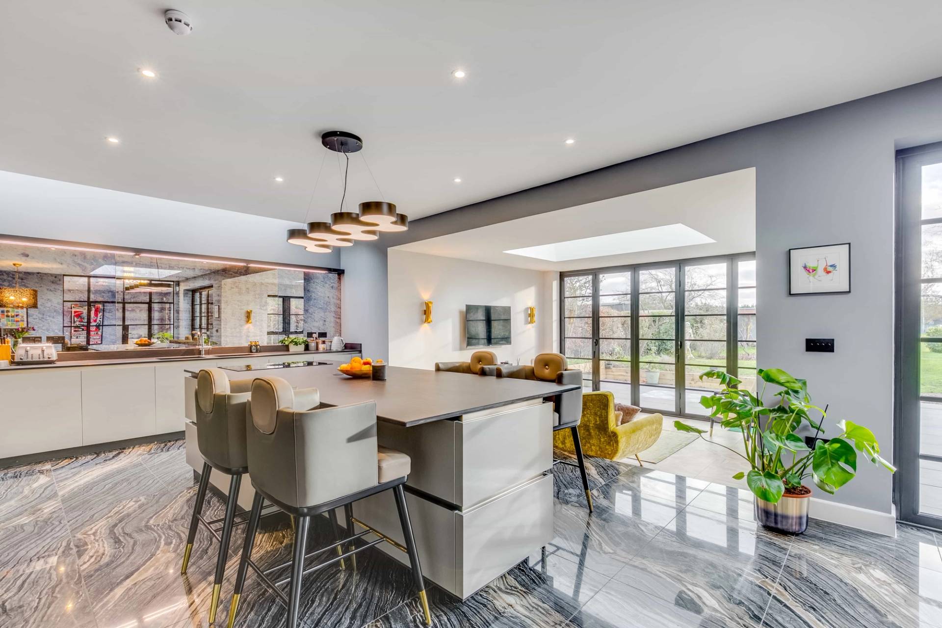Symmetrical open-plan kitchen island featuring light grey bar stools and contemporary pendant light, Love Locations CB2.