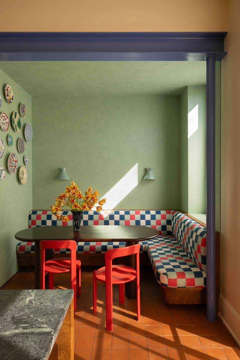 Cozy dining nook location house in Boerum Hill Brooklyn NY 11217 by Love Locations, displaying a red and white checkered corner banquette seat, sage green walls, and a black oval table with red chairs.