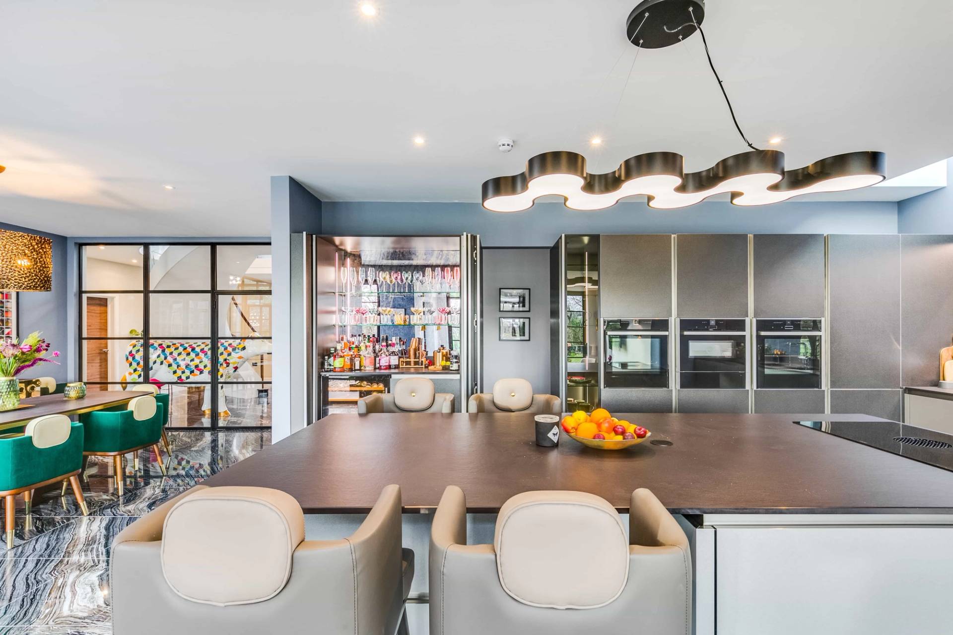 Contemporary kitchen island detail with light grey upholstered bar stools and wave pendant light, Love Locations CB2.