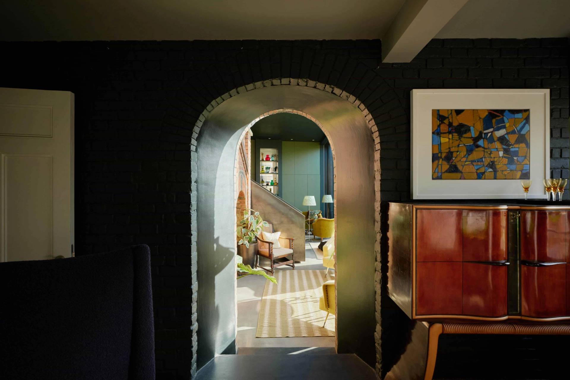 Dramatic dark living room looking through a yellow brick archway into a sunlit extension, ideal for feature film sets, Love Locations SW20.