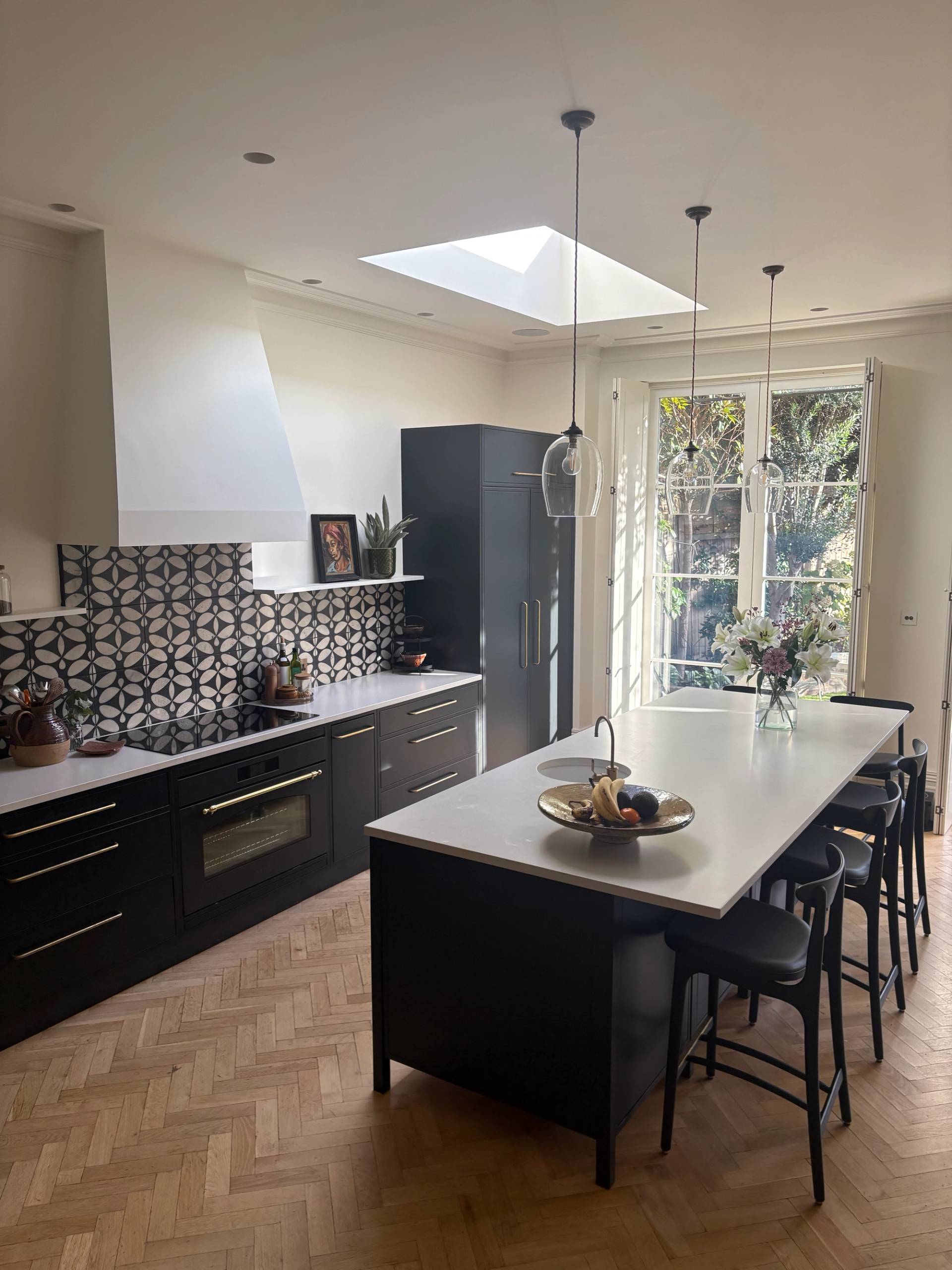 Wide angle view of a modern open-plan kitchen film location in Twickenham TW1 with a central island, breakfast bar seating, roof window, and French doors opening to the garden via Love Locations.
