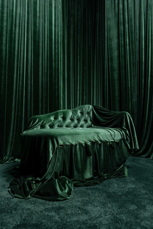 Close-up shot of a tufted emerald green velvet couch set against lush green velvet drapes for luxury brand campaigns, Love Locations N15.