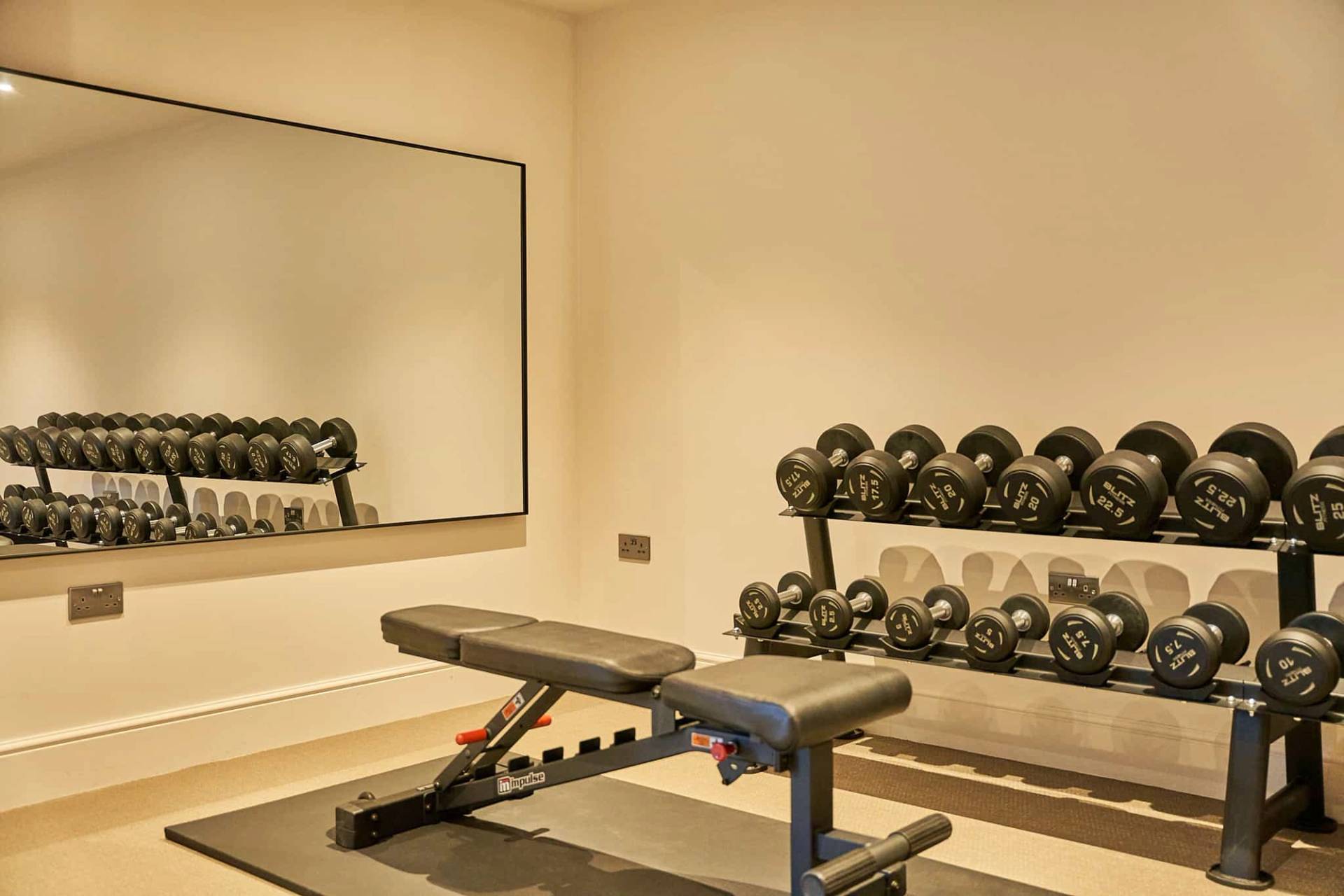 Home gym workout room with a weight bench, dumbbell rack, and large wall mirror, Love Locations SO21.