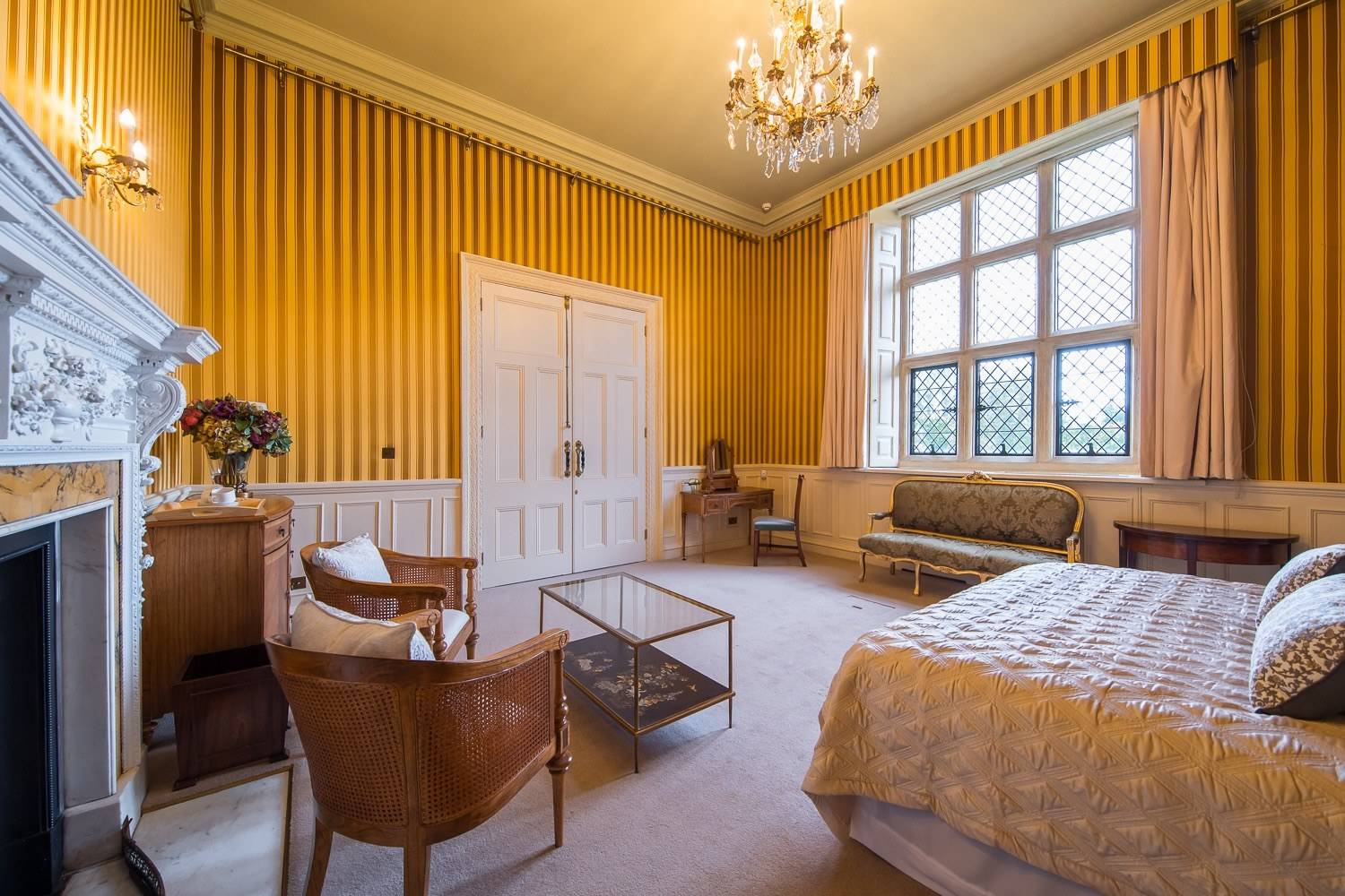 Bright period bedroom filming space with yellow striped walls, large lattice window, and neutral carpeting via Love Locations.