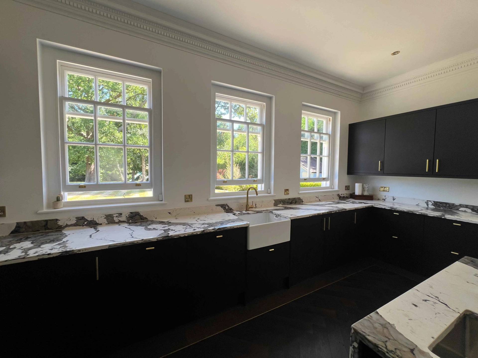 Black shaker kitchen cabinetry with white marble splashback, ceramic butler sink, and garden view windows, Love Locations BR7.