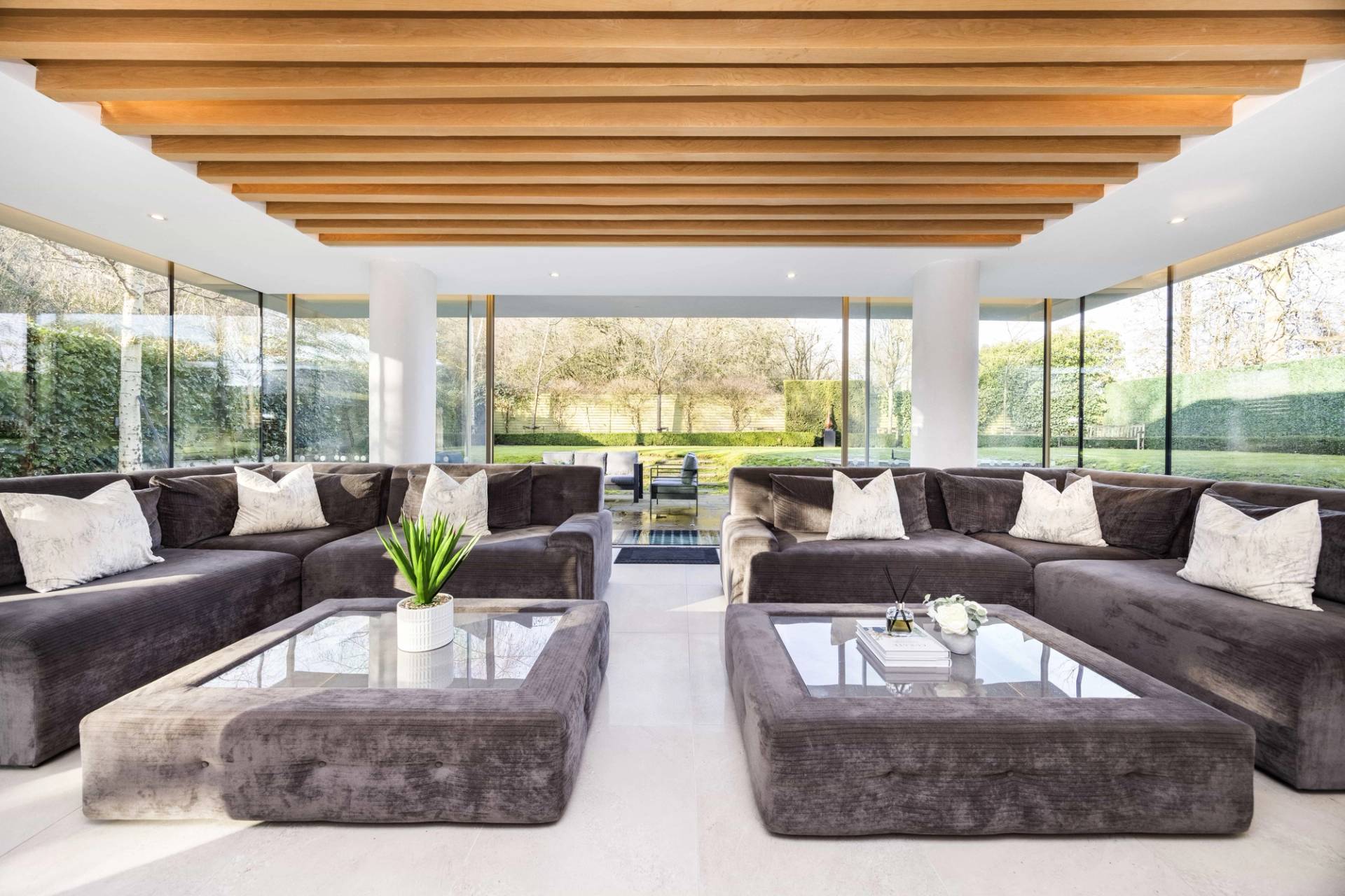 Symmetrical view of a grey velvet corner sofa set under an architectural slatted timber ceiling, Love Locations WD7.