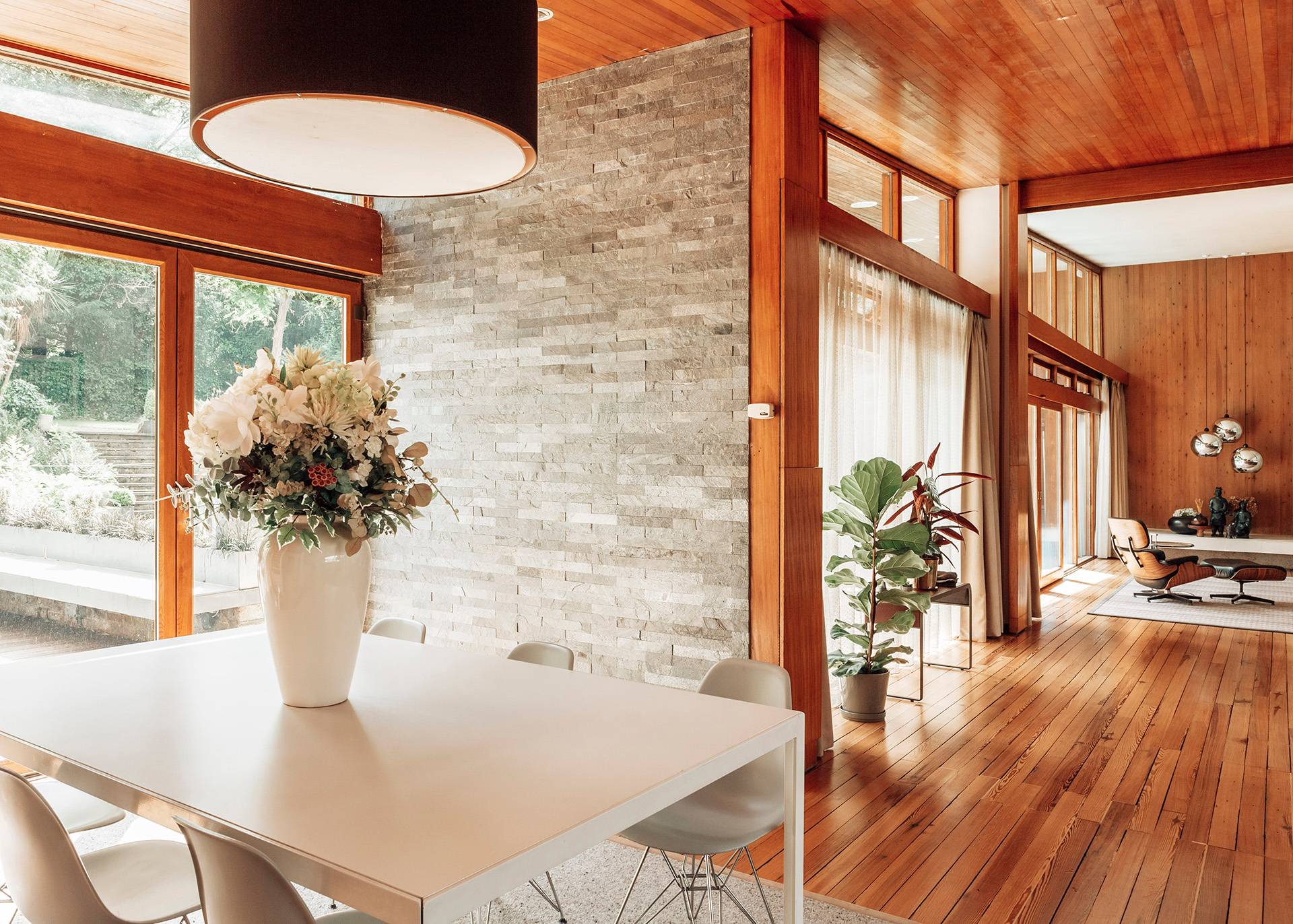 Bright dining space corner with a large vase of fresh flowers against a backdrop of natural wood panelling and garden views, Love Locations.