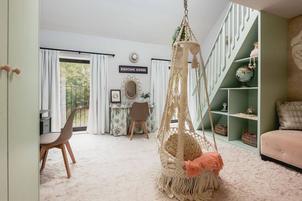 Playful bedroom interior with a hanging rattan egg chair, mint green ladder, and built-in shelving, Love Locations GU32.