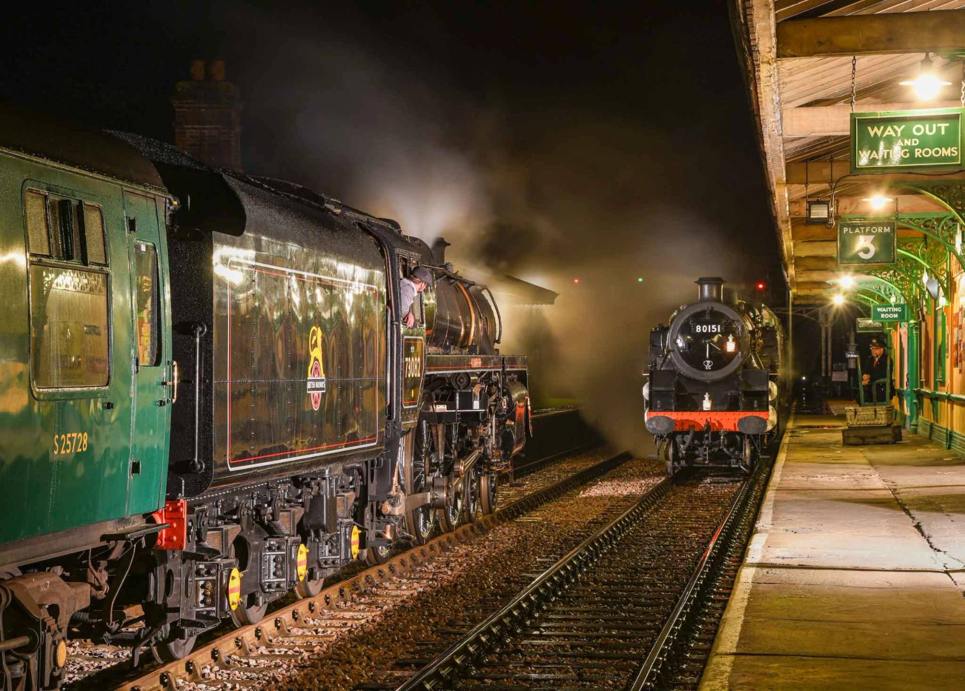 Atmospheric night shot of steam locomotives emitting smoke alongside a heritage station platform in Sussex, Love Locations.