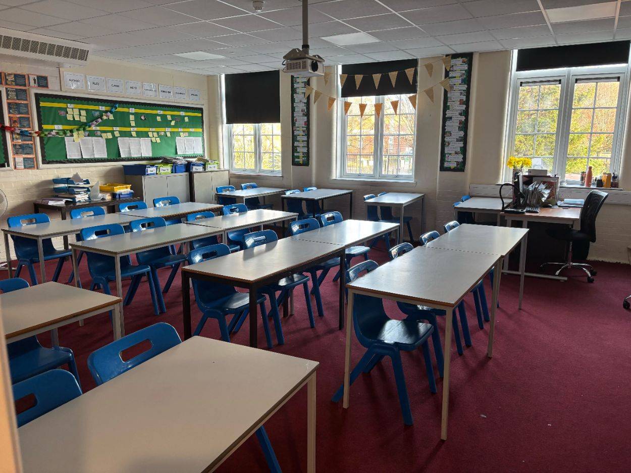 Classic school classroom film location in Sittingbourne Kent ME10, displaying wooden student desks, blue chairs, red carpet, and sash windows from Love Locations.