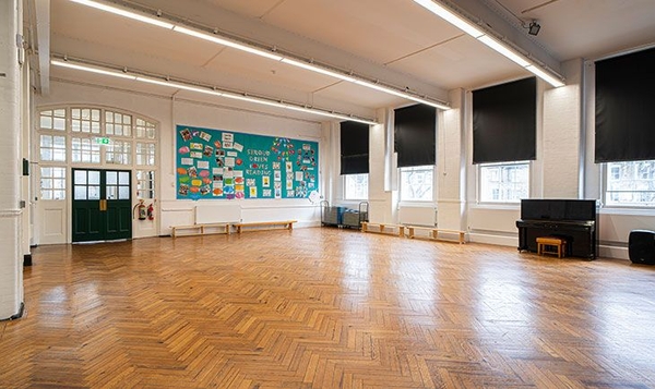 Large empty school hall studio with a colorful display board and blacked-out windows for controlled filming, Love Locations.