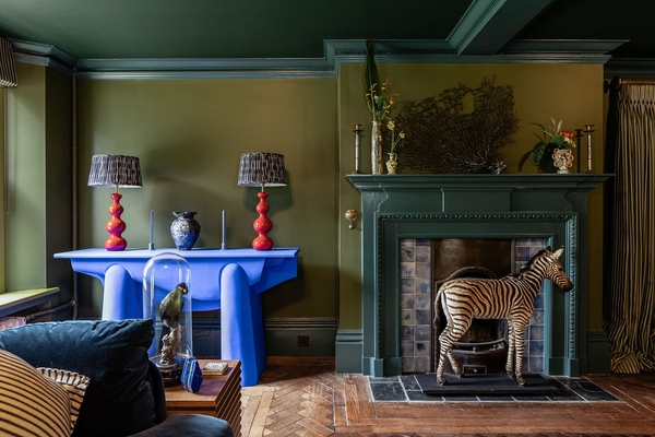 Dramatic drawing room film location in Liss Hampshire GU33 available via Love Locations, showcasing dark olive walls contrasting with a vibrant blue statement table and period fireplace.